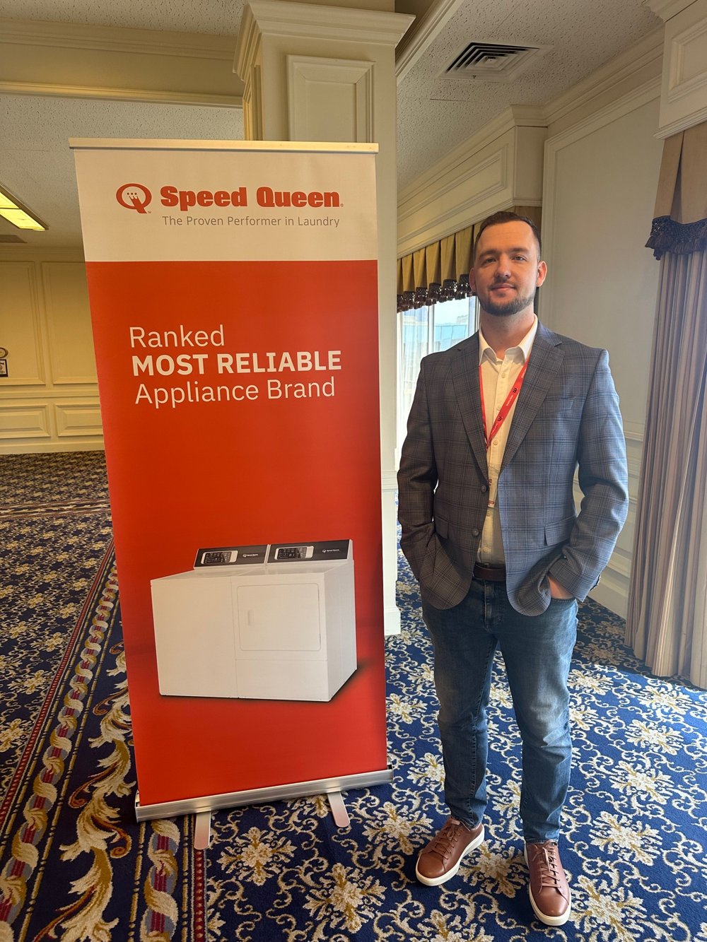 Egor Nikonov, owner of Appliance Service Pro, standing beside a Speed Queen banner at a training event